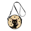 A round black cat cartoon graphic on a light wood background, attached to a black strap.