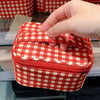 A hand is opening a red and white checkered makeup bag with a zipper on a shelf.
