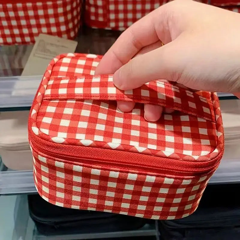 A hand is opening a red and white checkered makeup bag with a zipper on a shelf.