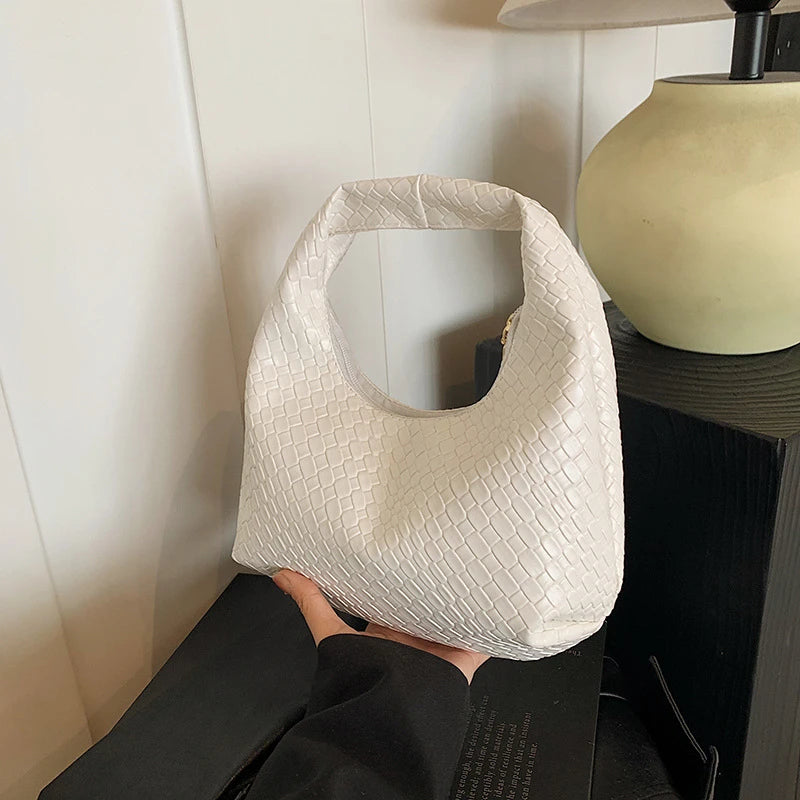 A close-up of a cream woven embossed hobo shoulder bag with a top handle being held by a person.