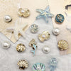 A collection of sea-themed jewelry charms including starfish, conch shells, and pearl accents on a light background.