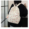 A white corduroy fashion backpack with a floral pattern and adjustable strap is worn by a person against a glass door.
