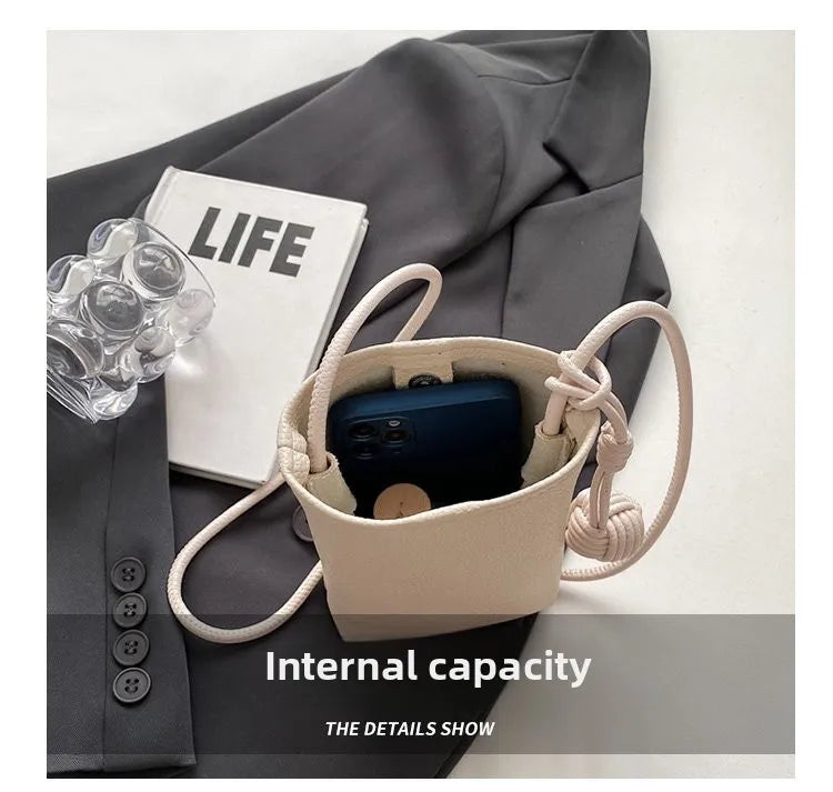 Bolso cruz de cuero beige con un smartphone oscuro sobre un fondo de tela gris.