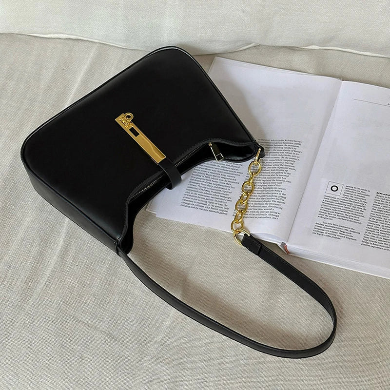 A black PU leather hobo shoulder bag with gold hardware resting on an open book.