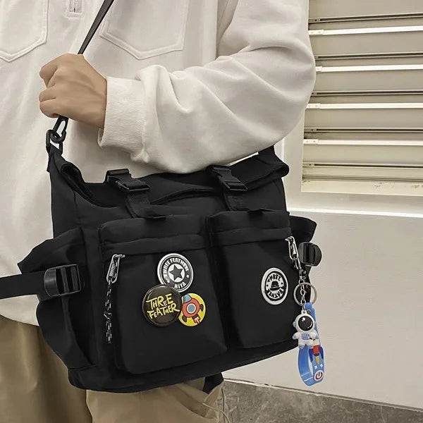 A black nylon crossbody bag with multiple pockets and charms is worn by a person.