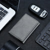 A gray magnetic leather card wallet resting on a dark surface next to a laptop and a keyboard.