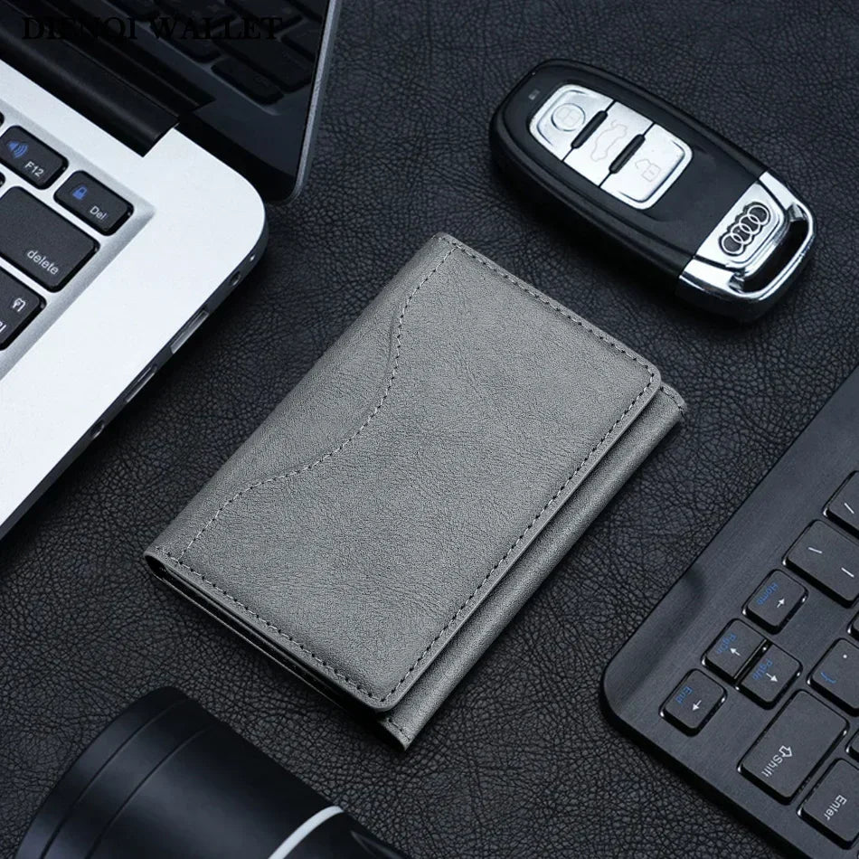 A gray magnetic leather card wallet resting on a dark surface next to a laptop and a keyboard.