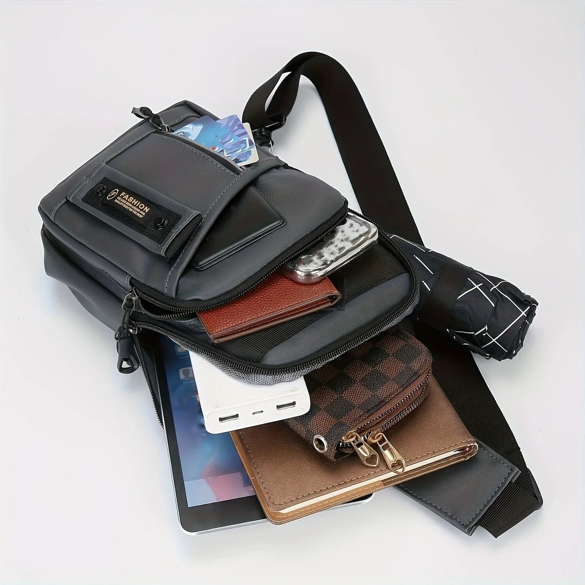 A black adjustable crossbody sling bag with multiple compartments and a strap is shown next to a smartphone and wallet.