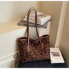 A brown leopard print vintage tote bag resting on a dark surface next to stacked books.