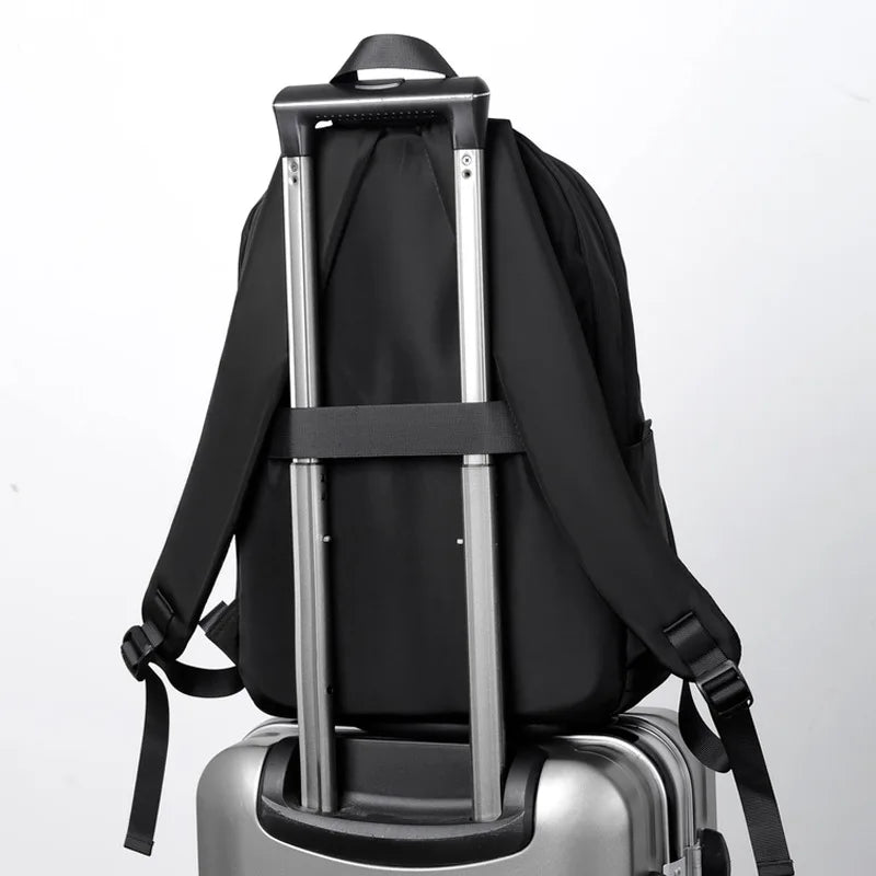 A black men's ultralight waterproof laptop backpack resting on a silver suitcase.