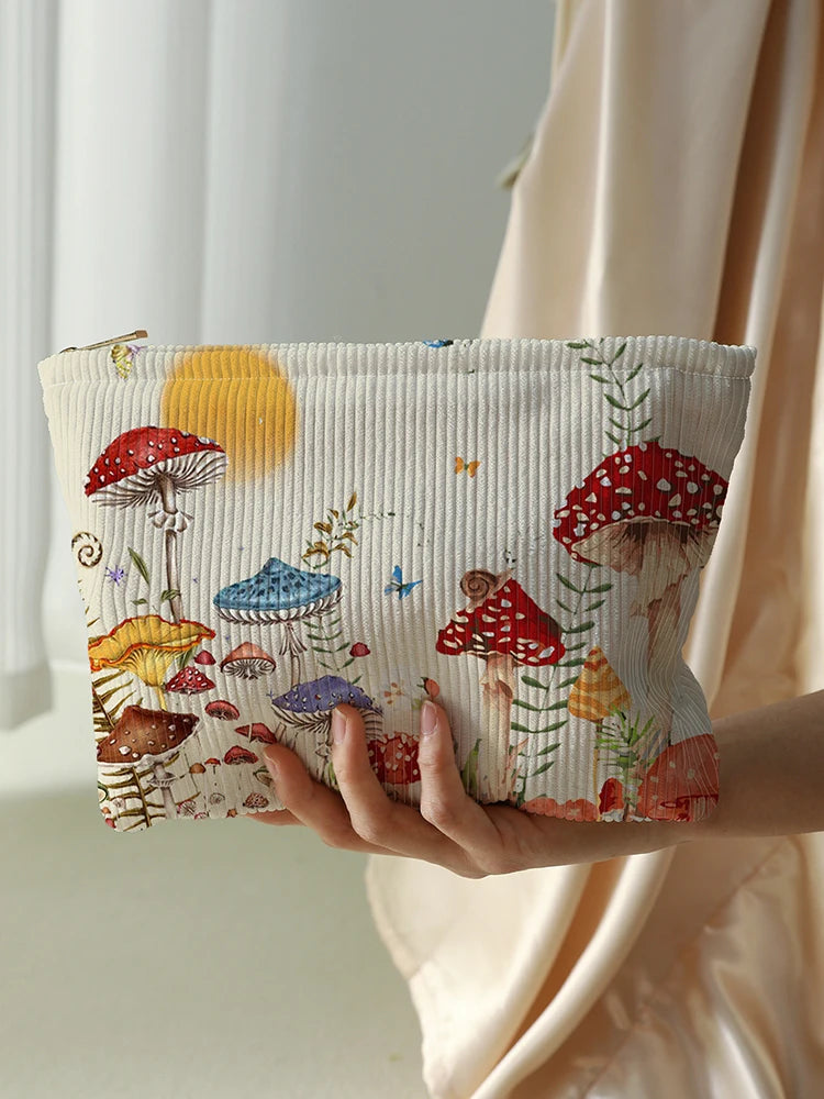 A beige makeup bag with a fairytale mushroom and butterfly print is held by a hand against a light curtain.