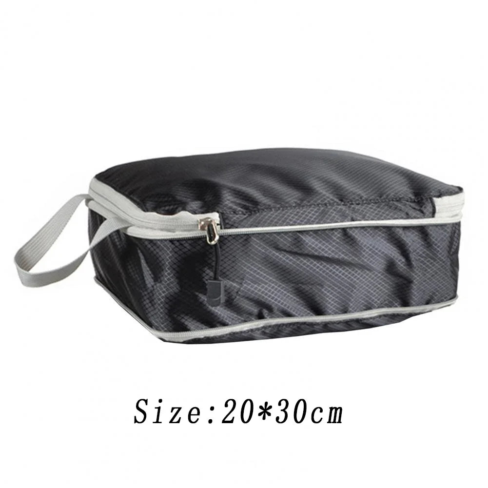 A black reusable compression packing cube with a light gray zipper and strap.