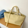 Sac à main en cuir PU beige clair, style décontracté, avec une poignée, posé sur une surface en bois.