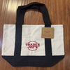 A white and black canvas tote bag with a red logo tag resting on the fabric.