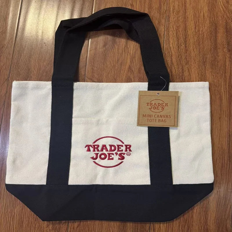 A white and black canvas tote bag with a red logo tag resting on the fabric.