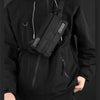 A person wearing a black hoodie with a black chest bag slung across the body.