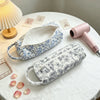 A light blue and white floral quilting storage bag is displayed on a white table next to a pink hair dryer.