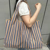 A person holds a striped grocery tote bag with vertical black, white, and brown stripes.
