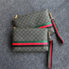 Dunkelgrabesprenkeltes Clutch-Handtasche mit grün-rotem Zierrand und schwarzem Riemen auf grauem Stoff