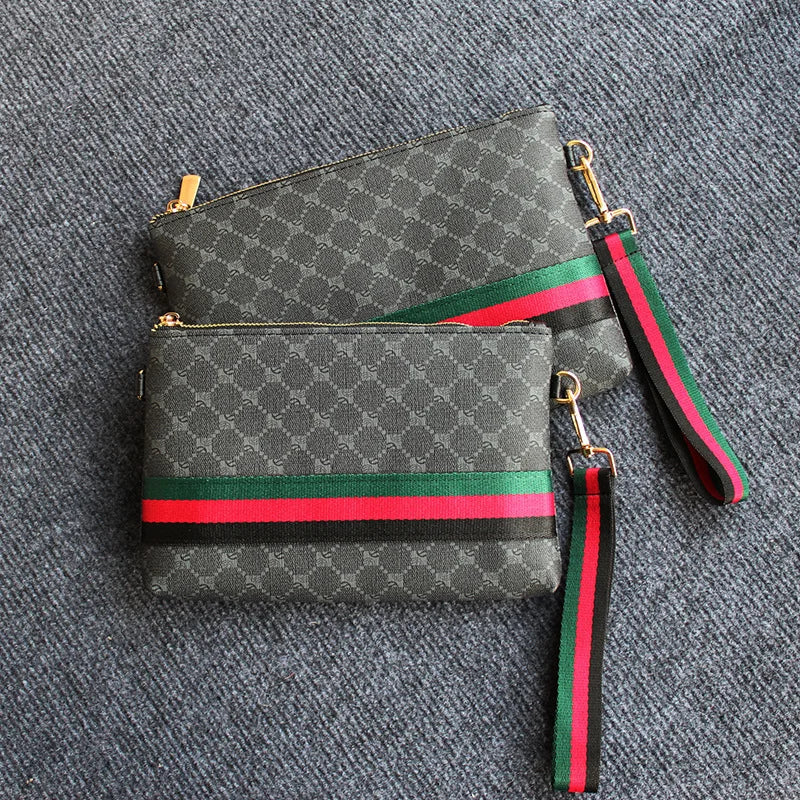 Dunkelgrabesprenkeltes Clutch-Handtasche mit grün-rotem Zierrand und schwarzem Riemen auf grauem Stoff