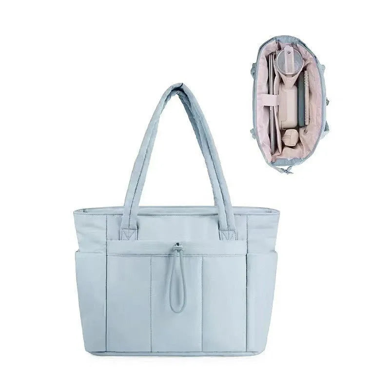 Light blue quilted tote bag with a leather interior pocket and strap shown against a white background.