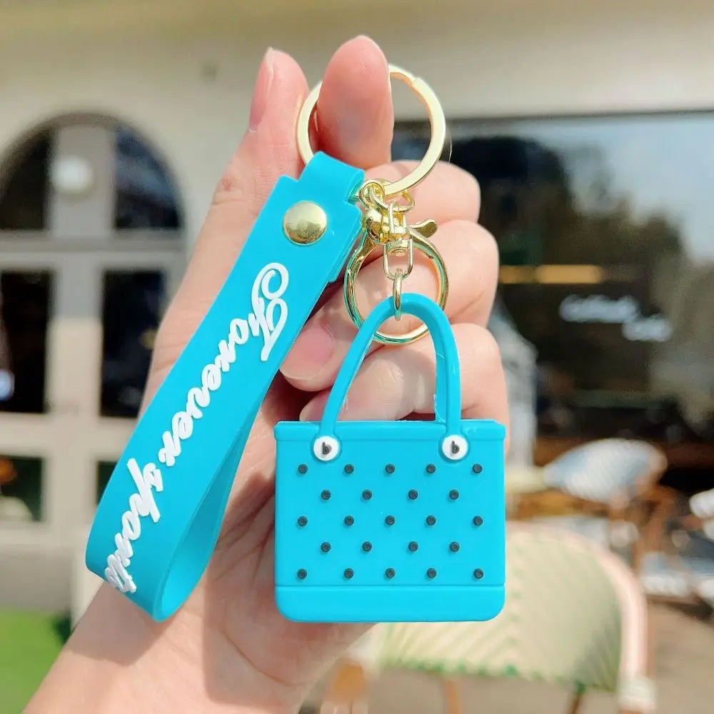 A hand holds a turquoise silicone heart beach bag keychain with a gold ring.