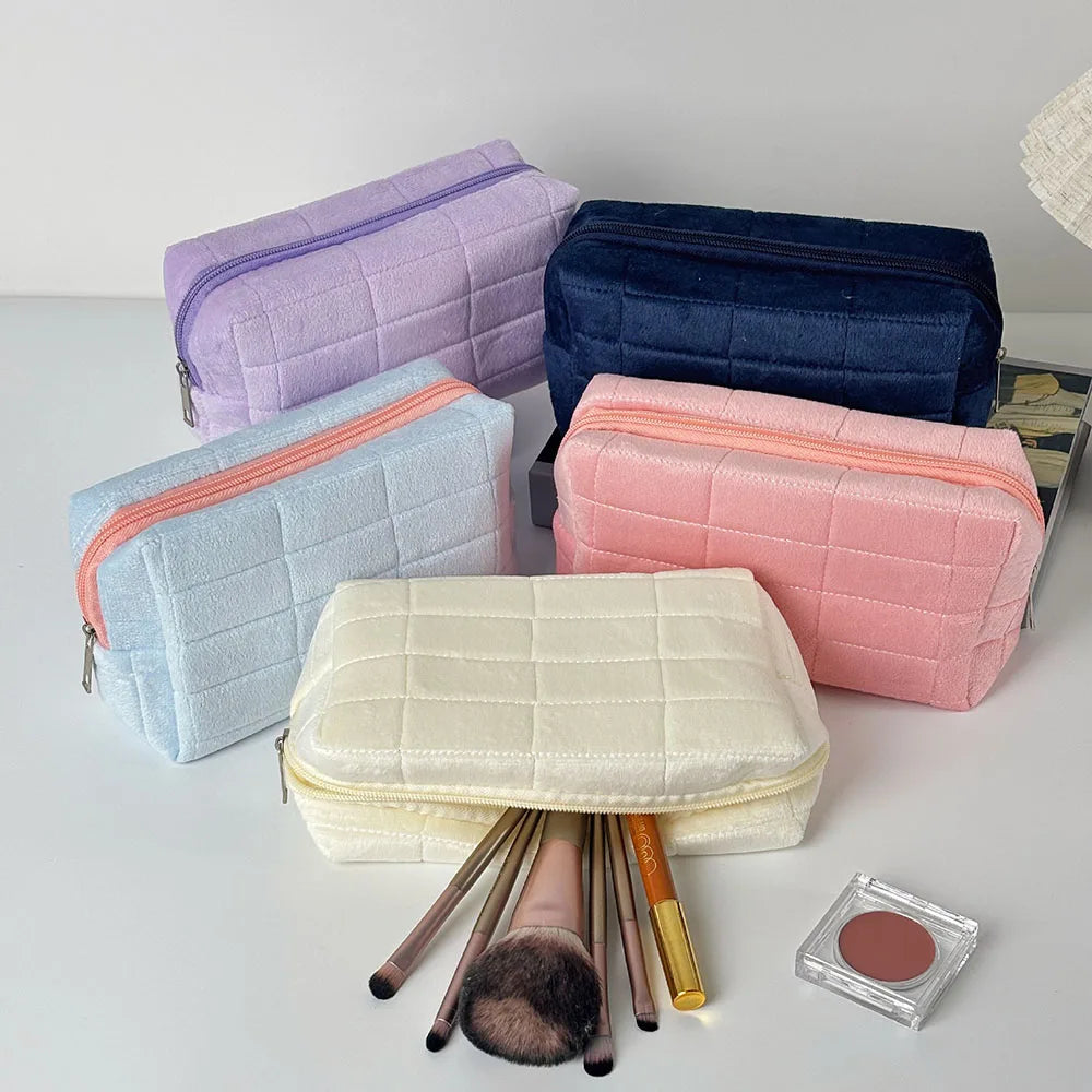 A collection of quilted velvet cosmetic and toiletry bags in purple, navy blue, light blue, and pink, with a gold-colored mak