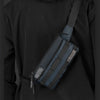 A dark gray chest bag is worn across the torso of a person in a black long-sleeved shirt.