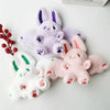A collection of soft stuffed bunny plush toys in purple, pink, and white colors.
