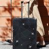 A black suitcase with an airplane pattern protector cover is being pulled by a person against a terracotta wall.