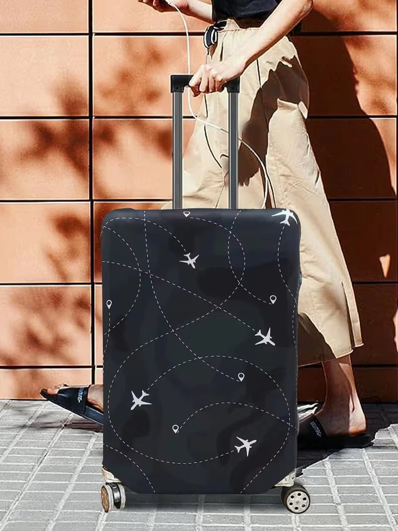 A black suitcase with an airplane pattern protector cover is being pulled by a person against a terracotta wall.