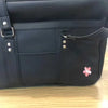 A black faux leather shoulder bag with multiple pockets and silver hardware resting on a wooden surface.
