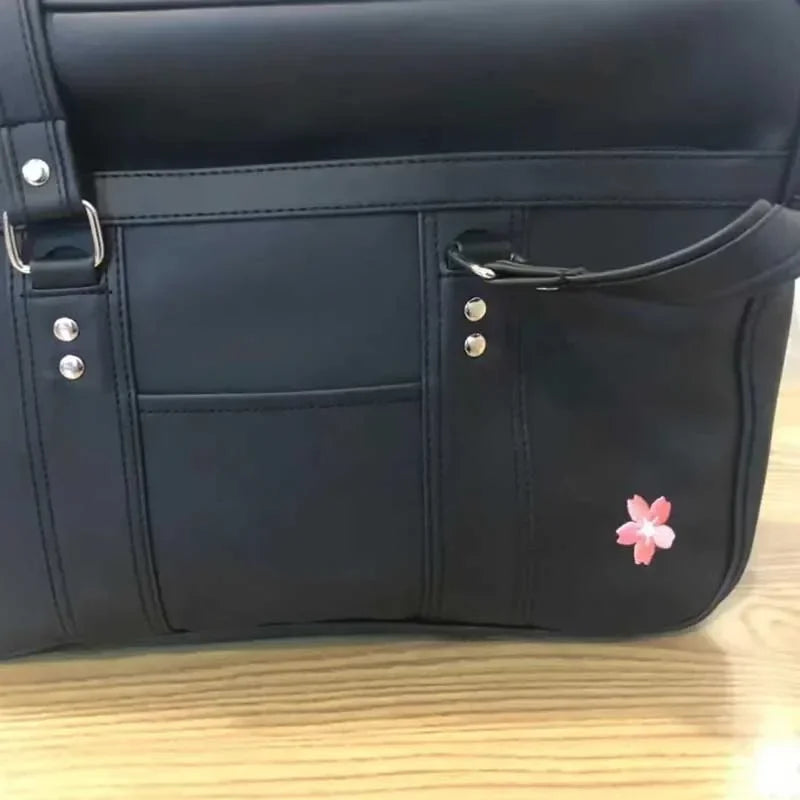 A black faux leather shoulder bag with multiple pockets and silver hardware resting on a wooden surface.
