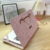 A pink PU laptop sleeve with a leather strap and silver chain is displayed on a wooden desk.