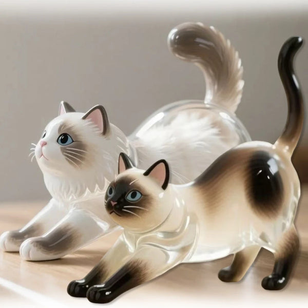A pair of white and brown ceramic cat figurines, one sitting and one lying down.