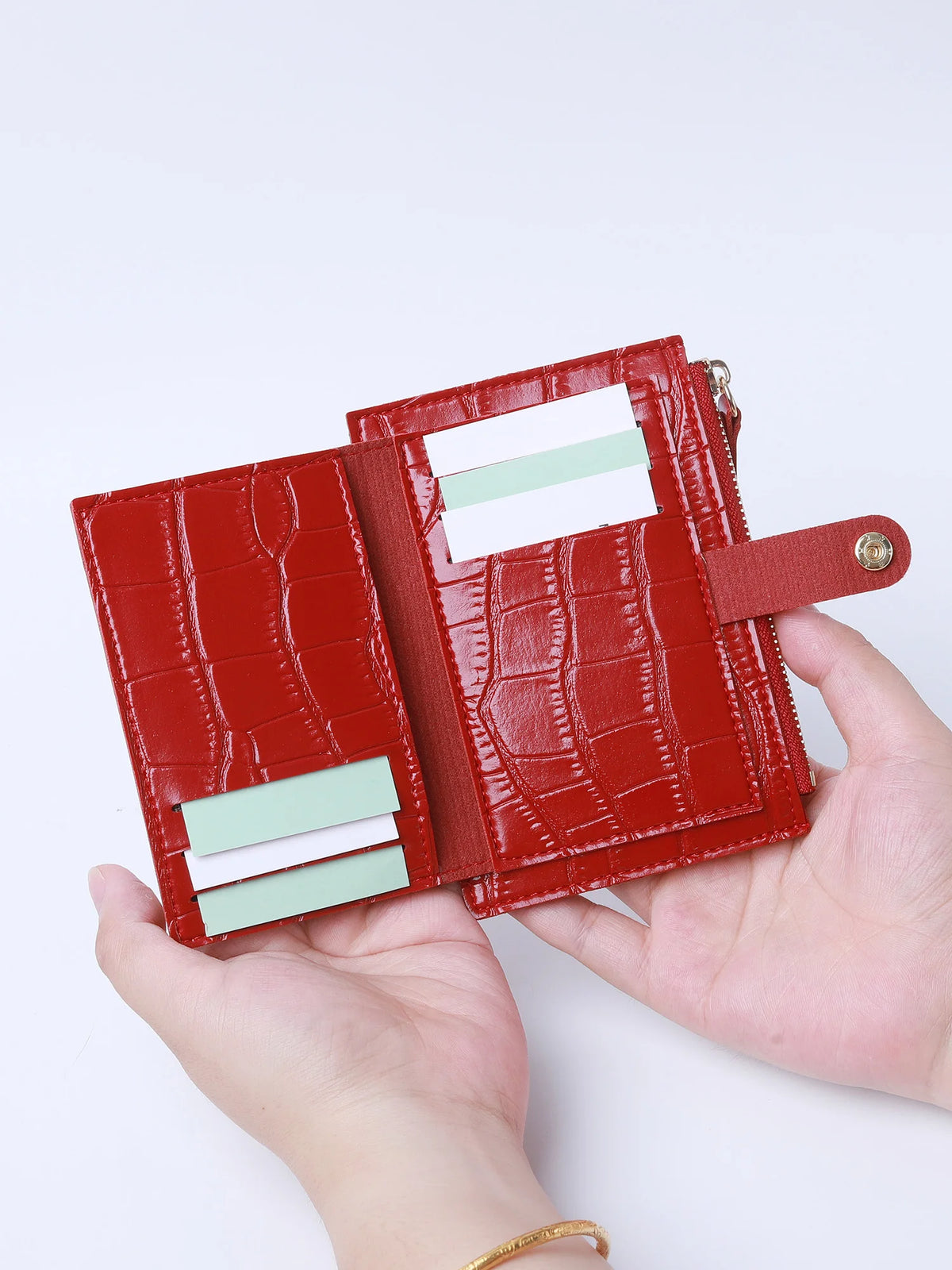A hand holds a red crocodile pattern leather card holder with a zipper, displaying several cards.