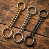 Three metal chain extenders or clasps in gold and silver tones laid on a wooden surface.