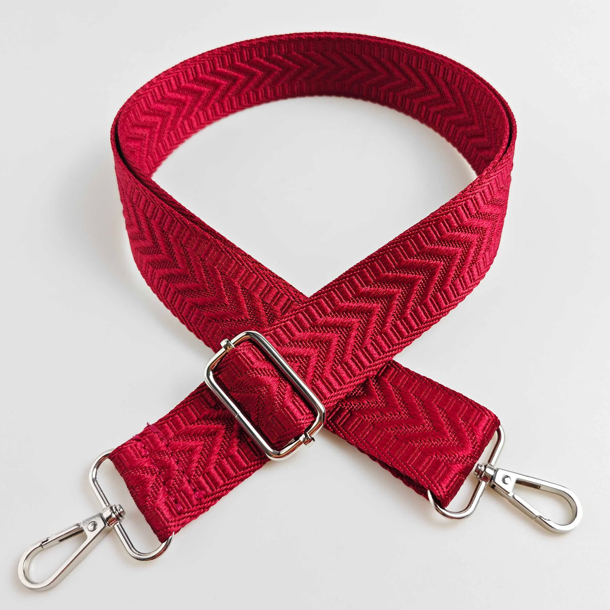 A red woven strap with an arrow jacquard pattern and silver hardware.