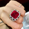 A hand is holding a luxury leopard crystal statement ring featuring a red gemstone surrounded by diamond accents.