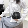 Una mujer modela un bolso cruz de cordón con pedrería negra brillante y cadena plateada contra una camisa blanca y falda gris