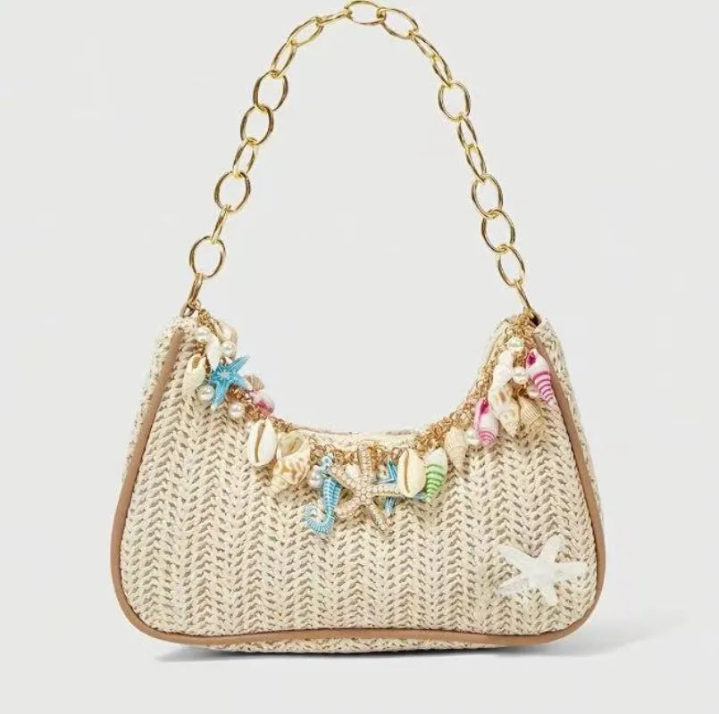 A beige woven straw shoulder bag adorned with colorful ocean charms and a gold chain strap.