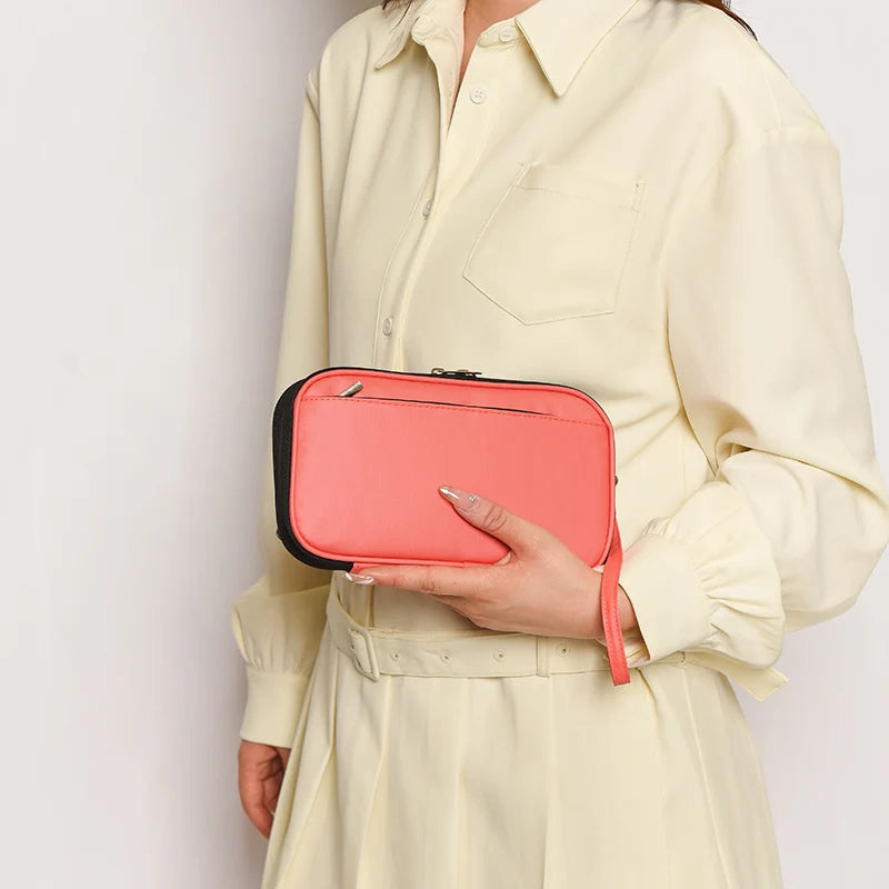 A woman wearing a cream shirt holds a coral pink multi-pocket travel document organizer.