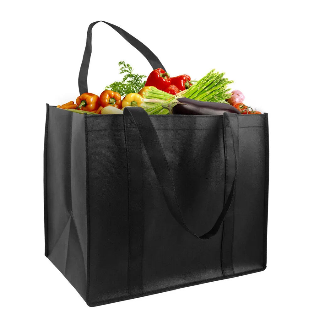 A black reusable eco-friendly tote bag filled with fresh vegetables like tomatoes and greens.