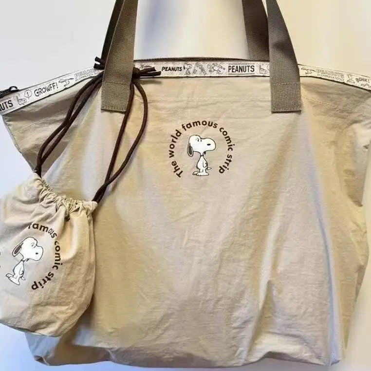 A light beige canvas shoulder bag featuring a Snoopy cartoon design and peanut branding.