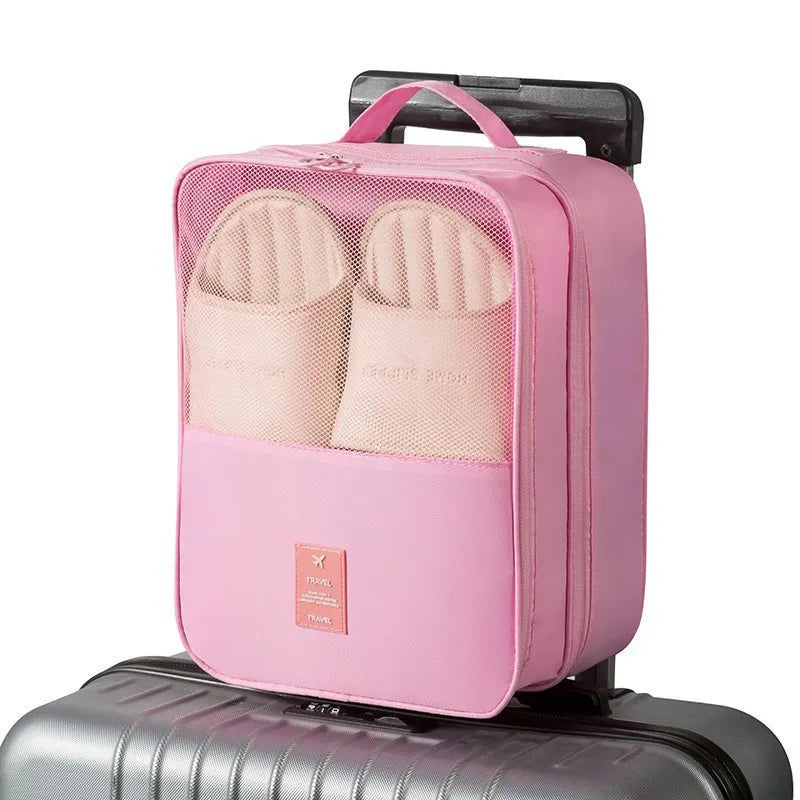 A pink portable luggage shoe organizer bag with multiple compartments resting on a gray suitcase.