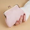 A pink velvet coin purse with a gold buckle is held by a hand against a beige background.
