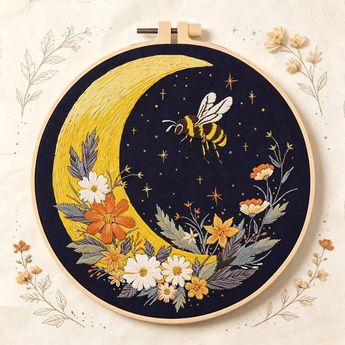 A dark fabric embroidery featuring a yellow crescent moon and floral elements, with a bee flying near the moon.