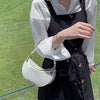 A woman wearing a black apron and white shirt holds a light gray leather handbag with a pearl strap.