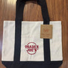 A black and white canvas tote bag featuring the Trader Joe's logo on the front.