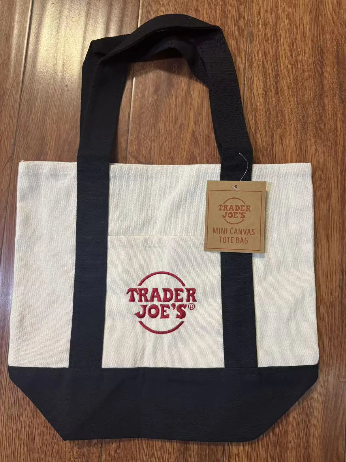 A black and white canvas tote bag featuring the Trader Joe's logo on the front.